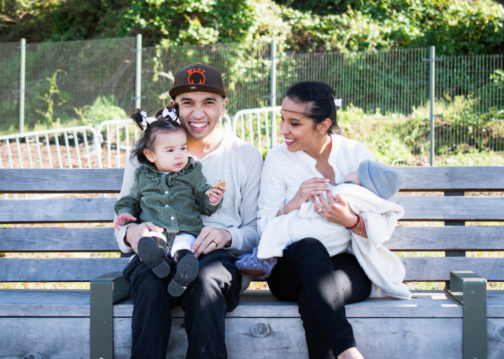 Happy family with two young children sitting on park bench