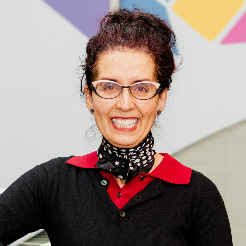 Headshot of a deputy director, wearing a black blouse with a red collar, and scarf, smiling at the camera.