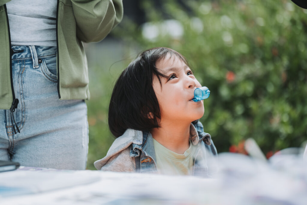 close up on young girl outside blowing a blue whistle