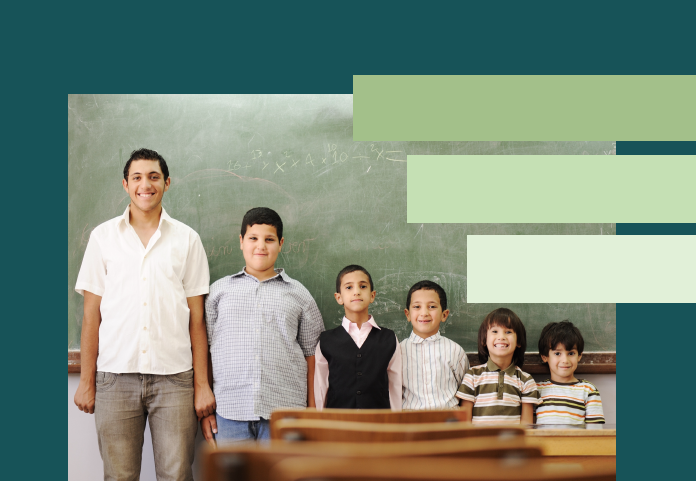 5 children ranging in age and height stand from tallest to shortest left to right in front of classroom chalk board