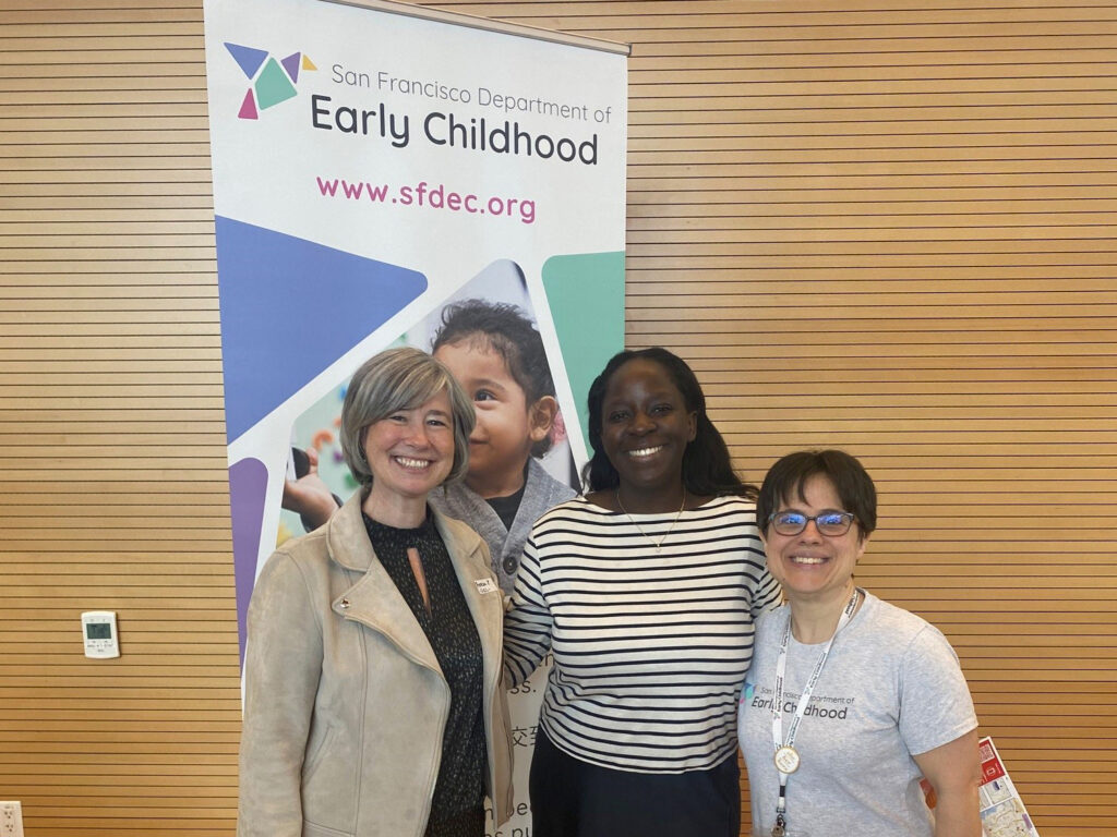 Three women stand in front of Department of Early Childhood vertical banner