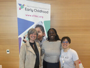 Three women stand in front of Department of Early Childhood vertical banner