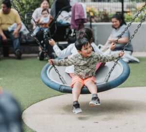 young boy on swing in park with other children